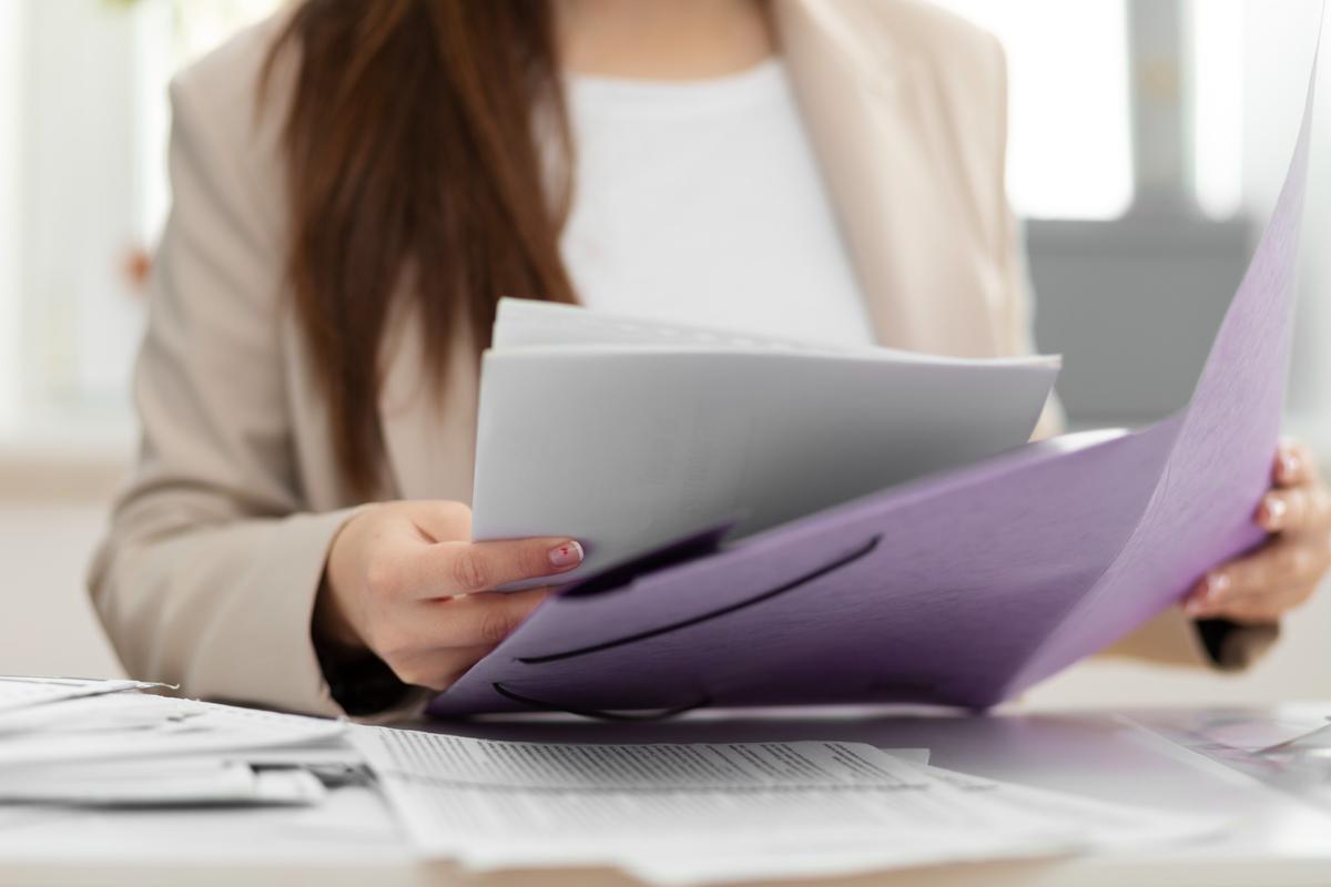 Mulher revisando documentos em uma pasta roxa sobre mesa de escritório, representando organização e gestão de arquivos.