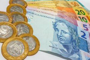 Imagem com moedas e cédulas de reais espalhadas, incluindo notas de 2, 5, 10, 20, 50 e 100 reais, representando o pagamento de RPVs pelo CJF.