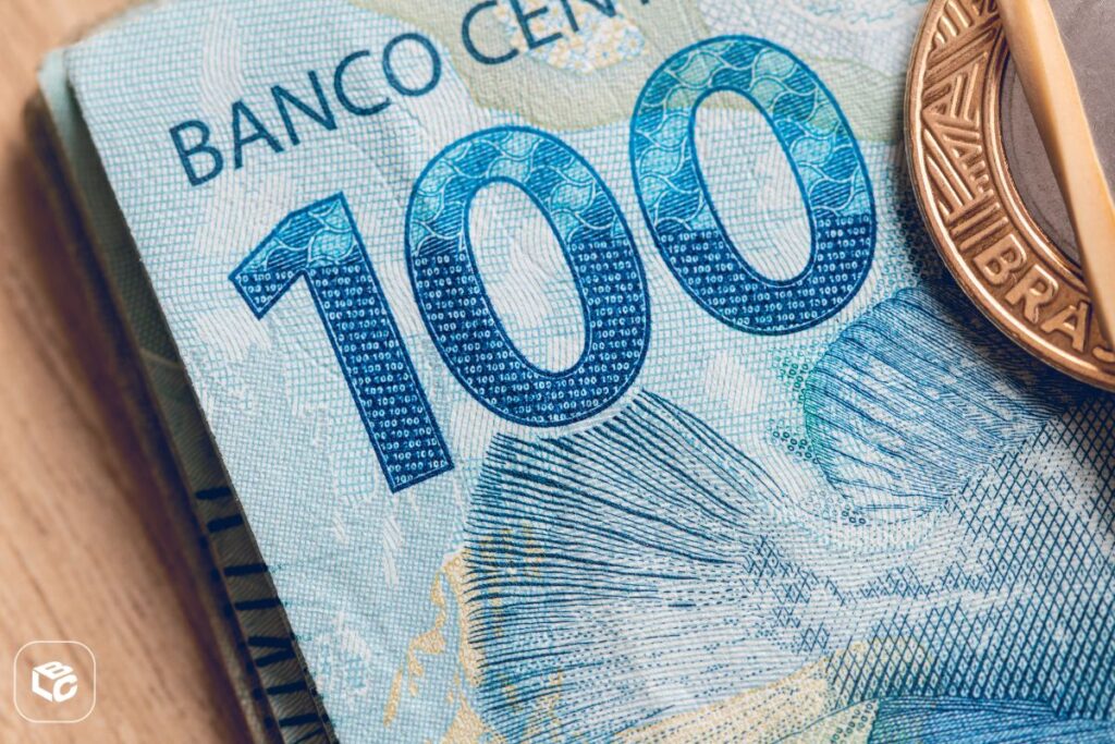 Nota de 100 reais e moeda, com foco no número 100