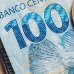 Nota de 100 reais e moeda, com foco no número 100