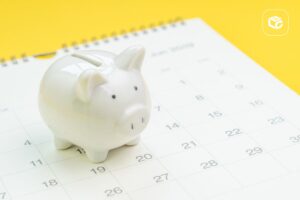 Cofrinho de porco branco sobre calendário, simbolizando a espera para antecipar RPV Federal.