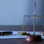 Balança da justiça dourada sobre papel e caneta, simbolizando direito e justiça.