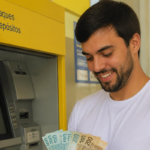 Homem sorri com dinheiro do Banco do Brasil em caixa eletrônico